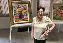 uma mulher parada ao lado de uma pintura na Exposição É Primavera