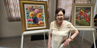 uma mulher parada ao lado de uma pintura na Exposição É Primavera