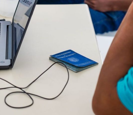 uma pessoa sentada em uma mesa com um laptop e uma carteira de trabalho